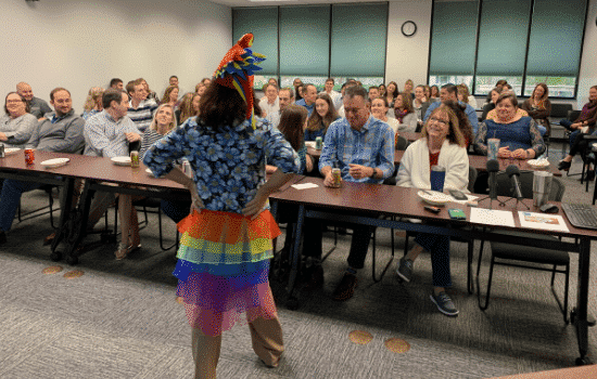 Suzanne Forbes in parrot hat and tailfeathers in front of JMCO Gainesville staff
