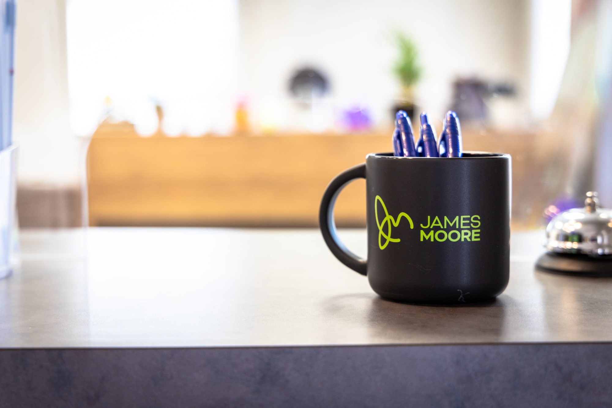 Coffee cup sitting on a counter top with three blue pens in it.