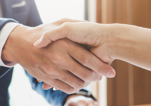Close-up of a handshake between a person in a navy blazer and a person in a white shirt.